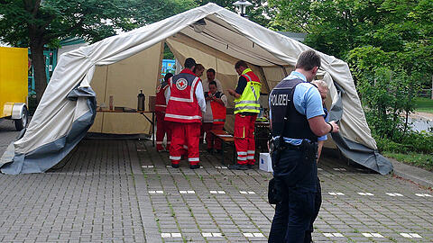 Polizisten stehen am 19.07.2015 in Halberstadt (Sachsen-Anhalt) vor einem Rot-Kreuz-Zelt, das neben einer Sporthalle steht, in der Asylsuchende untergebracht sind. Zuvor waren Helfer des Deutschen-Roten-Kreuzes von Jugendlichen, die "Ausländer raus" skandierten, mit Steinen beworfen worden.