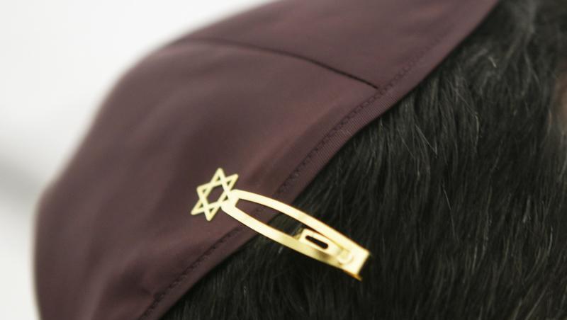 Ein Jude hat sich bei den Feierlichkeiten einer Grundsteinlegung für eine Synagoge seine Kippa mit einer Davidstern-Klammer am Haar befestigt.