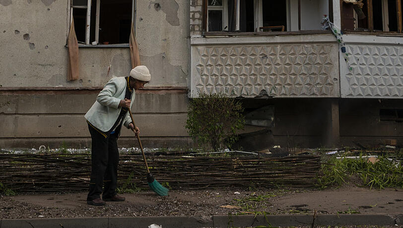 Eine Frau kehrt die Trümmer auf, nachdem russische Soldaten ihr Wohngebäude beschossen haben.