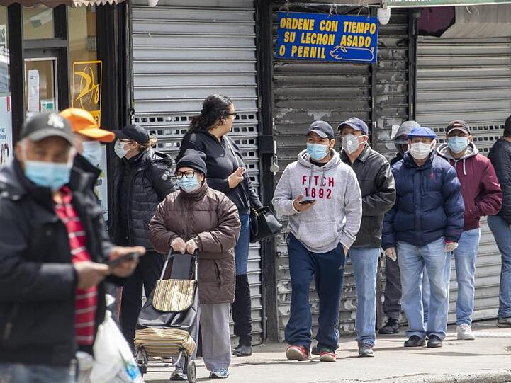 Menschen mit Mundschutz stehen in einer Schlange vor einem Lebensmittelgeschäft im New Yorker Stadtteil Queens.