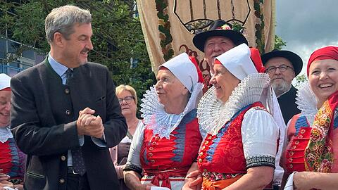 Bayerns Ministerpräsident Markus Söder (CSU, l) steht vor Beginn der Hauptkundgebung des Sudetendeutschen Tages zwischen Mitgliedern einer Trachtengruppe.