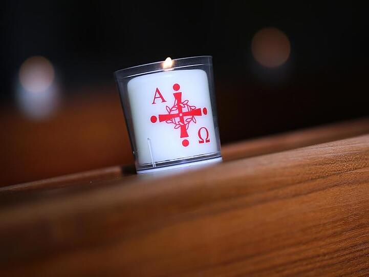 Eine brennende Kerze mit dem Aufdruck Alpha und Omega (für Anfang und Ende. Foto: Ronny Hartmann/dpa/Symbolbild