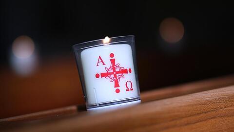 Eine brennende Kerze mit dem Aufdruck Alpha und Omega (für Anfang und Ende. Foto: Ronny Hartmann/dpa/Symbolbild