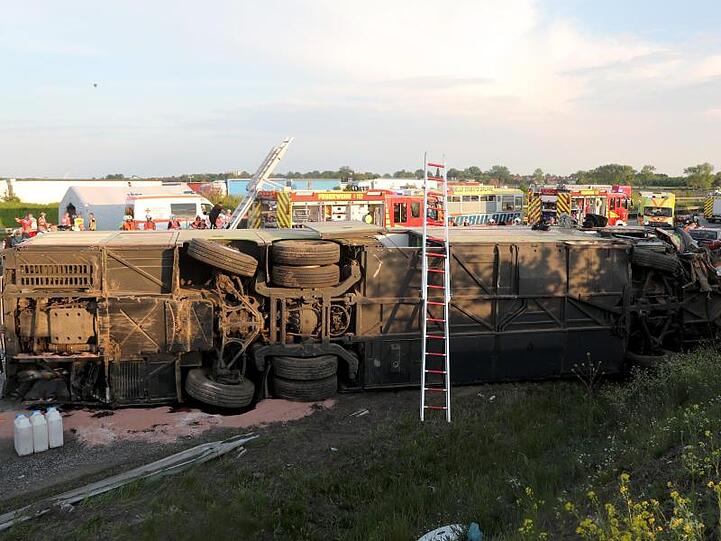 Einsatzkräfte der Feuerwehr stehen an der Unfallstelle neben dem verunglückten Bus. Der Bus überschlug sich zwischen den Anschlussstellen Leipzig-West und Bad Dürrenberg. Anschließend blieb das Fahrzeug auf der Seite liegen.