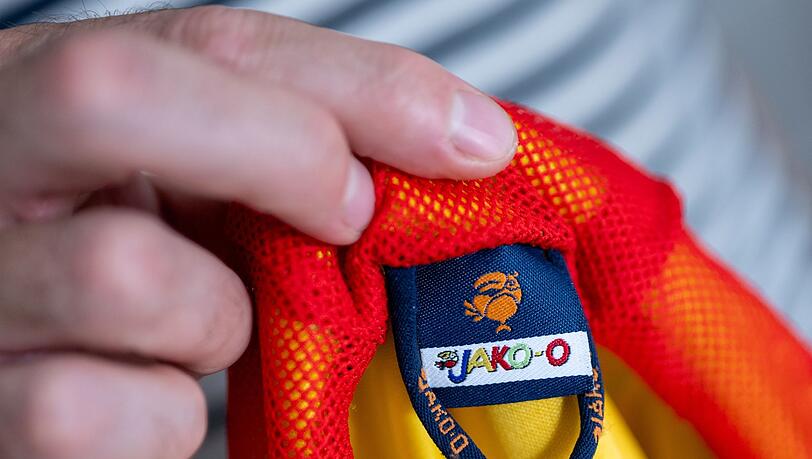 Ein Mann hält eine Kinderjacke der Modemarke Jako-o in der Hand.