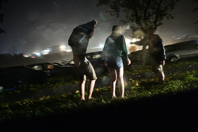 Drei Festivalbesucherinnen stehen nach der Unwetterwarnung im Regen am Straßenrand.