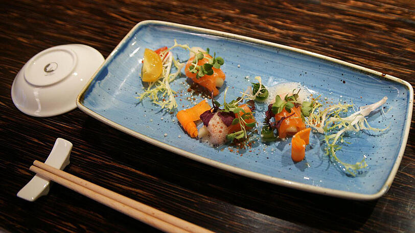 1. Gang: Wildlachs-Sashimi mit grünem Apfel, getrockneter Sojabohne und Yuzu-Trüffel-Sauce Hauchdünne Köstlichkeiten, ein wunderbarer Auftakt zum Menü &ndash; die feinen Aromen kann der leichte Vinho Verde &bdquo;Falco da Raza&ldquo; vom portugiesischen Weingut Quinta da Raza mit etwas Apfel und seinem Süß-Säure-Spiel unterstützen.