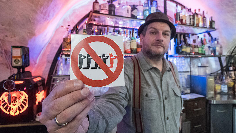 Kneipier Martin Stein zeigt in Regensburg einen Aufkleber, der auf die Junggesellenabschiedsfreie Zone in seiner Bar hinweist.