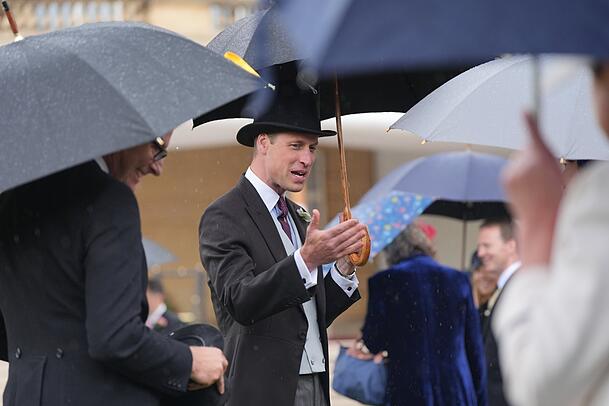 Trotz des starken Regens zeigt er sich heiter bis sonnig: Prinz William (ein paar Kilo hat er abgenommen) spricht mit Gästen während der Garten-Party vorm Buckingham-Palast.