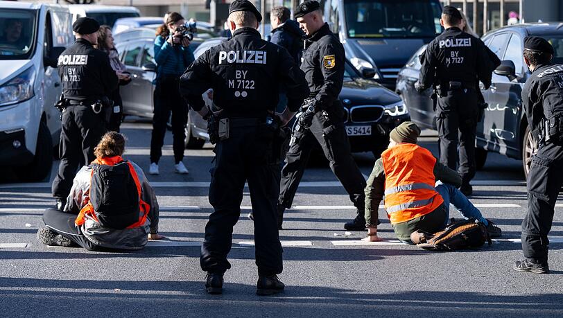Polizeibeamte stehen neben Klimaaktivisten, die sich am Karlsplatz auf die Fahrbahn geklebt haben.