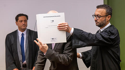 Die Anwälte Ömer Sahinci (l) und Adam Ahmed (r) stehen bei ihrem Mandanten im Gerichtssaal. Der 57-Jährige ist angeklagt, vor 24 Jahren seine damals 28 Jahre alte Ehefrau und Mutter seiner vier Kinder, die sich von ihm getrennt hatte, gemeinsam mit einem Komplizen getötet zu haben.