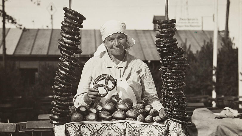 Eine Verkäuferin von Brezn und Salzweckerl steht vor einem Bierzelt auf dem Festgelände des Münchner Oktoberfests im Jahr 1921.