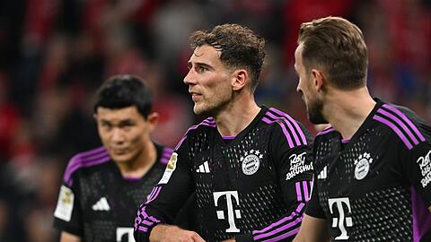Münchens Leon Goretzka (M) steht mit Harry Kane (r) sowie Minjae Kim zusammen und fasst sich an die Hand.