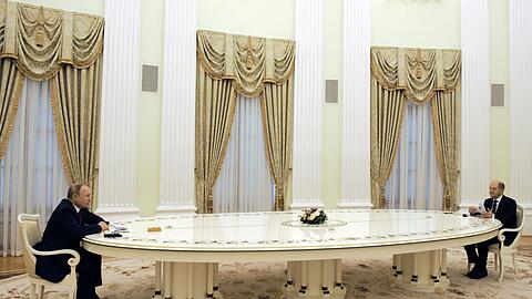 Russlands Präsident Wladimir Putin (links) und Bundeskanzler Olaf Scholz (SPD) sitzen sich an einem langen Tisch im Kreml gegenüber.