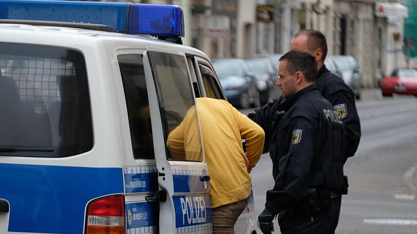 Beamte der Bundespolizei begleiten einen Mann zu einem Polizeifahrzeug. In einem Mehrfamilienhaus im Stadtteil Plagwitz fand ein Polizeieinsatz im Zusammenhang mit Scheinehen statt.