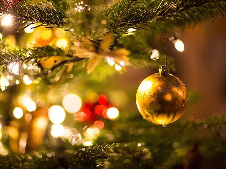 Eine goldene Kugel hängt an einem Weihnachtsbaum auf dem Weihnachtsmarkt. Foto: Friso Gentsch/dpa/Archivbild