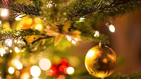 Eine goldene Kugel hängt an einem Weihnachtsbaum auf dem Weihnachtsmarkt. Foto: Friso Gentsch/dpa/Archivbild