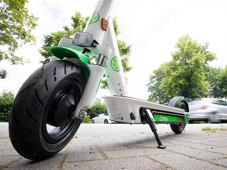 Ein E-Tretroller zum Mieten steht auf einem Parkplatz am Straßenrand. Foto: Christian Charisius/Archivbild