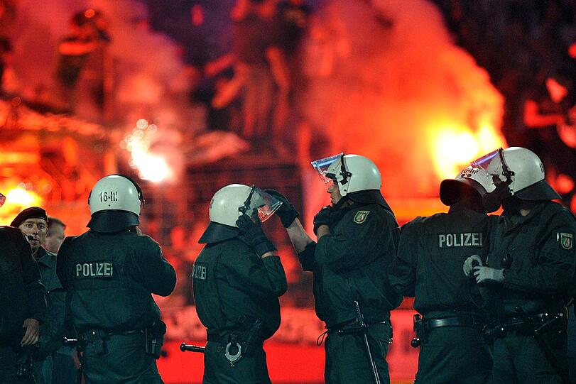 Polizisten beziehen nach Abfiff Aufstellung auf dem Feld, während Fans auf der Tribüne Bengalos abbrennen.