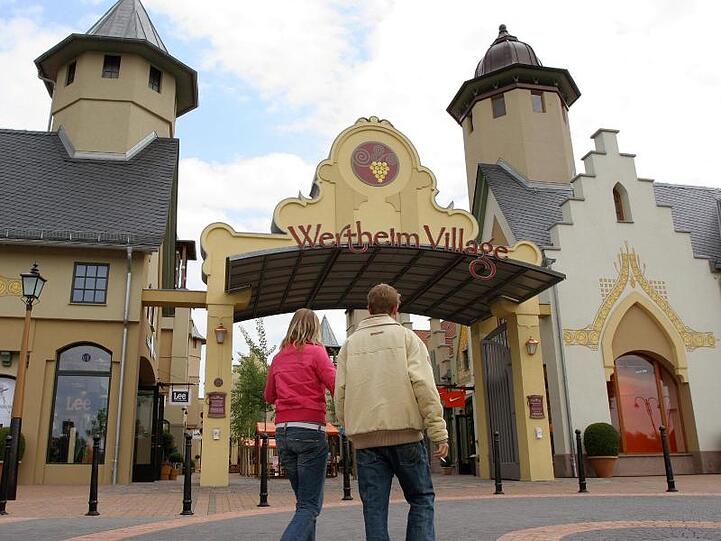 Besucher gehen zum Eingang des Factory-Outlet "Wertheim Village". Foto: Heiko Wolfraum/dpa/Archivbild