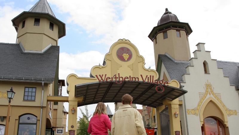 Besucher gehen zum Eingang des Factory-Outlet "Wertheim Village". Foto: Heiko Wolfraum/dpa/Archivbild Besucher gehen zum Eingang des Factory-Outlet "Wertheim Village". Foto: Heiko Wolfraum/dpa/Archivbild