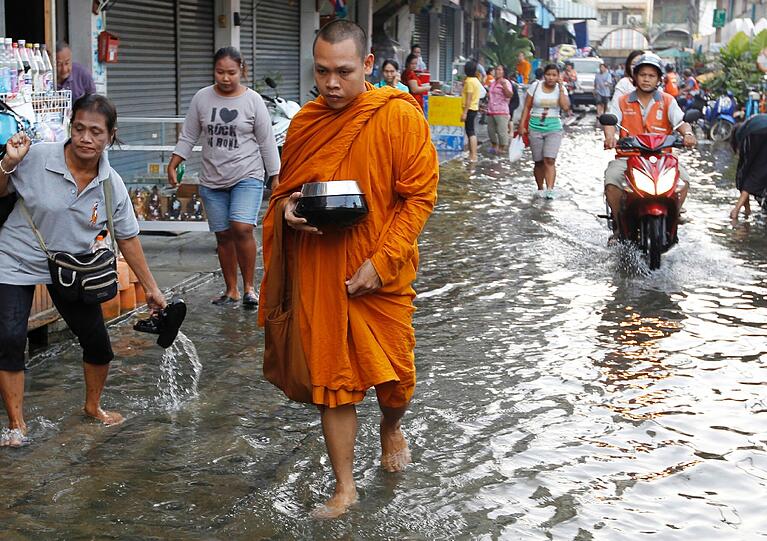 Ein buddhistischer Mönch watet durch eine überflutete Straße.