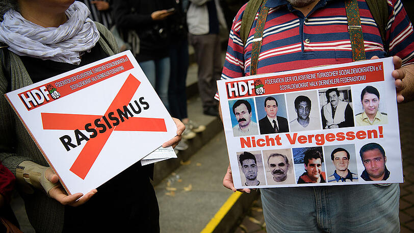 Teilnehmer der Demo halten ein Schild mit den Bildern der Opfer der NSU sowie ein Schild mit dem durchgestrichenen Schriftzug "Rassismus" in den Händen.