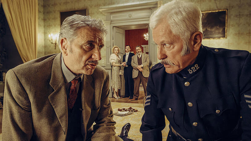 Chief Inspector Francis Lightmyer (Udo Wachtveitl, li.) und Constable Ivor Partridge (Miroslav Nemec, re-) untersuchen Arthur im Kaminzimmer. Lady Bantam (Sunnyi Melles, hinten, l-r), Charles (Ferdinand Hofer) und Dr. Mallard (Alexander H&ouml;rbe) beobachten sie - eine Szene aus &bdquo;Tatort: Mord unter Misteln&ldquo; (2022).