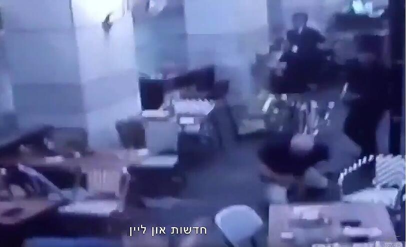 Aufnahme der Überwachungskamera: Einer der Attentäter (beide im Anzug) schießt auf einen älteren Mann. Getroffen sinkt er auf die Knie.