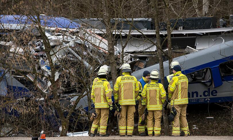 Einsatzkräfte der Bad Aiblinger Feuerwehr stehen vor einem der Zugwracks.