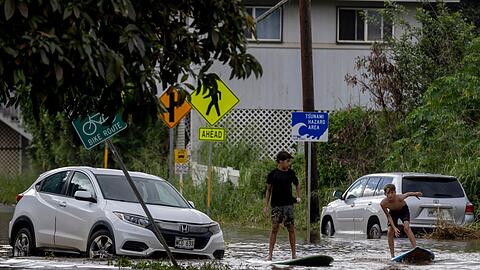 Zwei Jugendliche surfen in Waialua neben einem liegengebliebenen Fahrzeug im Hochwasser.
