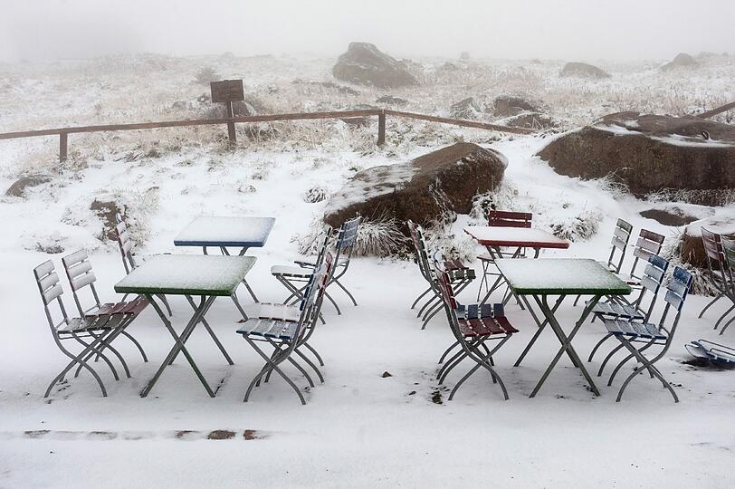 Verschneite Stühle und Tische stehen am Samstag auf dem Brocken im Nationalpark Hochharz in der Nähe von Wernigerode im ersten Neuschnee nach dem Sommer.