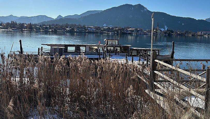 Gut getarnt hinter Pflanzen: Der ehemalige Ausflugsdampfer MS Bad Wiessee liegt auf dem Tegernsee bereits mit Wasser vollgelaufen schief am Steg. Das Landratsamt Miesbach hat den Besitzer aufgefordert, ihn zu entfernen.