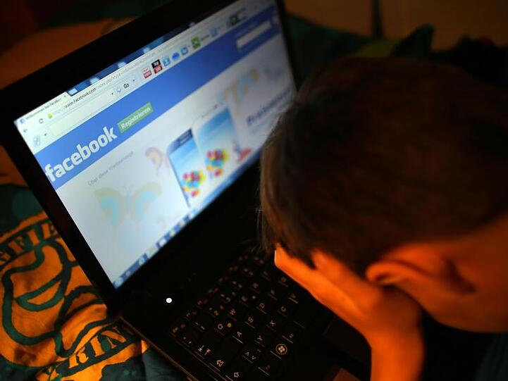 Ein Junge reibt sich am vor seinem Laptop beim Betrachten der Facebook-Seite die Augen. Foto: Oliver Berg/dpa/Archivbild