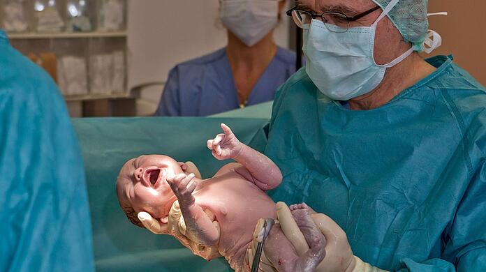 Ein Baby kommt in einem Kreißsaal in Erlangen zur Welt. Die von Gesundheitsminister Karl Lauterbach angestoßene Krankenhausreform könnte unter anderem zur Schließung zahlreicher Geburtshilfestationen führen.