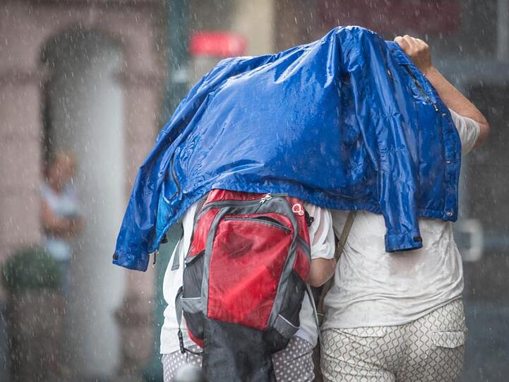 Mit einer Jacke versuchen sich zwei Frauen während eines Unwetters vor dem Regen zu schützen. Foto: Boris Roessler/Archivbild