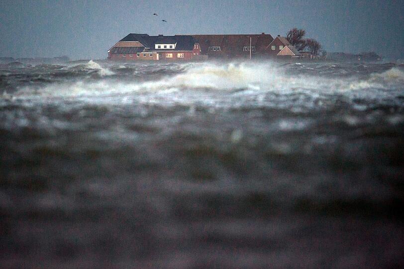 Häuser sind am 06.12.2013 auf der nordfriesischen Hallig Langeneß (Schleswig-Holstein) hinter hohen Wellen der Nordsee zu sehen.