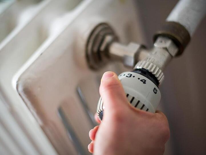 Eine Frau dreht am Thermostat einer Heizung. Foto: Ole Spata/Archiv