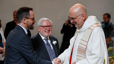 Pfarrer Siegfried Thuringer (r.) beglückwünscht Ex-Mönch Anselm Bilgri (M) und seinen Mann Markus Bilgri nach der kirchlichen Hochzeit in der alt-katholischen Kirche St. Willibrord.