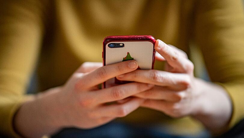 Eine junge Frau hält ein Smartphone in der Hand.
