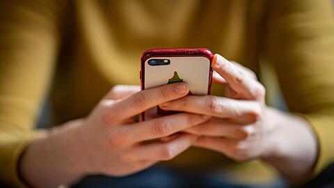 Eine junge Frau hält ein Smartphone in der Hand.