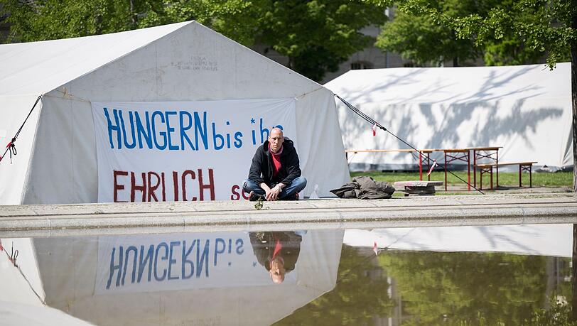 Wolfgang Metzeler-Kick sitzt am neuen Standort des Hungerstreik-Camps des Bündnisses "Hungern bis ihr ehrlich seid" im Regierungsviertel vor einem Banner.