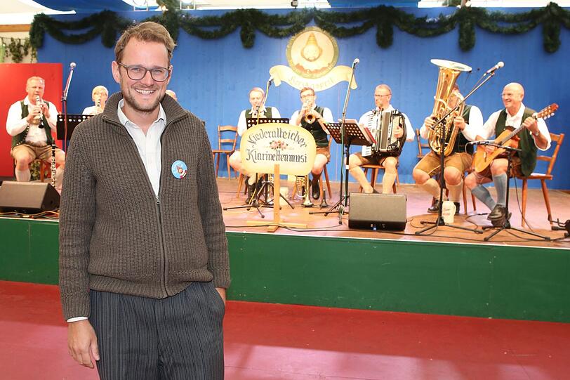 Martin Jonas, der Musik-Chef vom Herzkasperl-Festzelt: Im Hintergrund auf der Bühne spielen Musikanten zur Mittagswiesn auf.