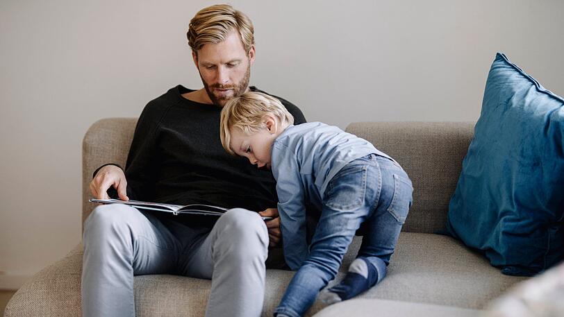 Vater und Sohn sitzen auf der Couch (Symbolfoto).