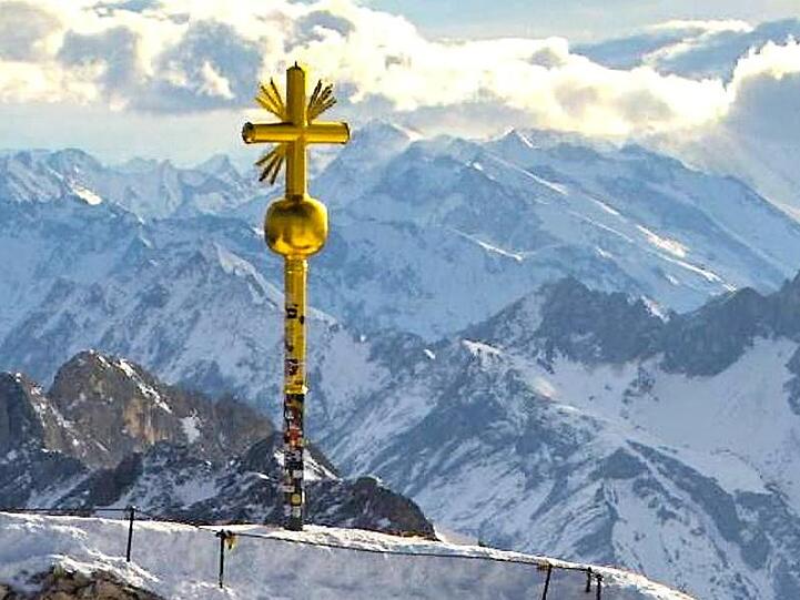 Das Gipfelkreuz auf der Zugspitze, an dem rechts unten einige vergoldete Strahlen abgebrochen sind. Foto: Bayerische Zugspitzbahn