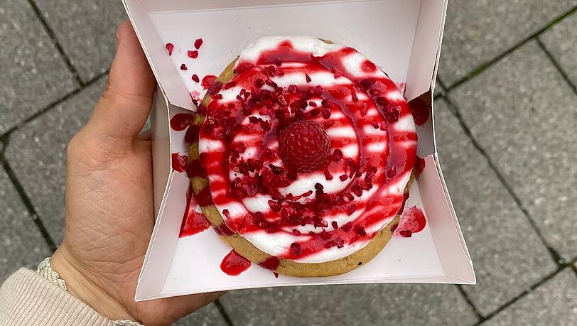 Der "Raspberry White Chocolate-Cookie" ist mit reichlich Vanille-Frosting und Himbeerpüree verziert. Der "Raspberry White Chocolate-Cookie" ist mit reichlich Vanille-Frosting und Himbeerpüree verziert.