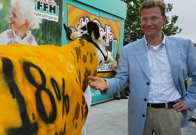 Guido Westerwelle (FDP) steht 2002 in Bad Vilbel neben einer gelb bemalten Kuh mit der Aufschrift "18 Prozent mehr Milch".