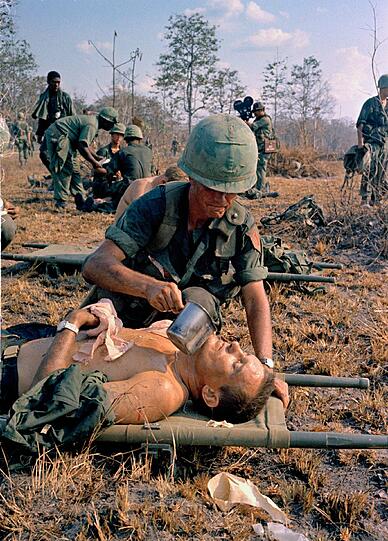 Ein verletzter amerikanischer Soldat bekommt Wasser auf einem Schlachtfeld (1967).