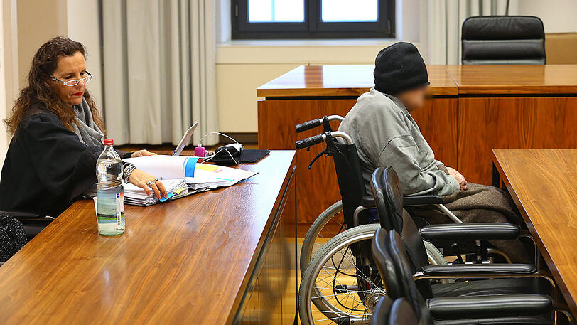 Hans K. sitzt in einem Rollstuhl im Gerichtssaal des Landgerichtes Memmingen vor seiner Rechtsanwältin Anja Mack.