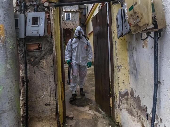 Ein Mann mit Schutzkleidung und einem Gerät zur Straßendesinfektion in einem Armenviertel von Rio de Janeiro.